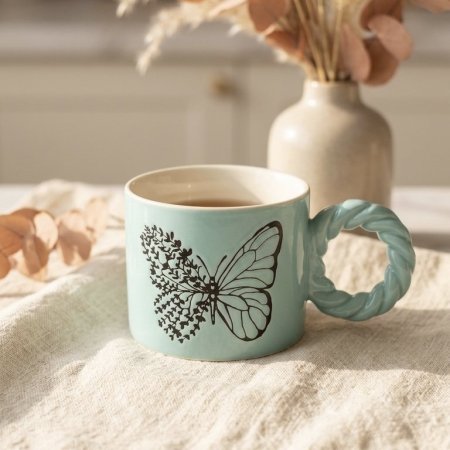 مج سيراميك اررق بنقش فراشة سوداء مع يد بشكل ملتف